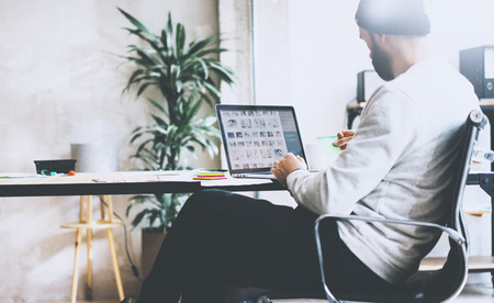 Picture bearded hipster working with new project modern loft. Using contemprary laptop on wood table. Creative process. Freelance world. Blurred background, film effectの写真素材