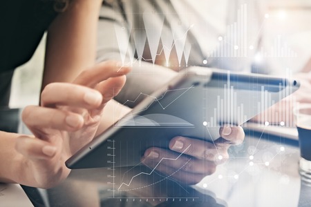 Closeup photo female hands holding modern tablet. Account managers working new private banking project office. Using electronic devices. Graphics icons, worldwide stock exchanges interface.の写真素材