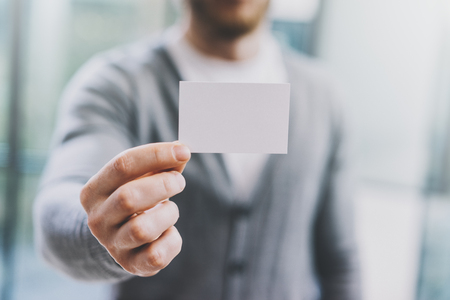 Man wearing casual shirt and showing blank white business card. Blurred abstract background. Horizontalの写真素材