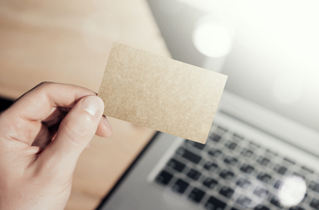Closeup Photo Man Showing Blank Craft Business Card and Using  Modern Laptop Blurred Background. Mockup Ready for Private Information. Sunlight Reflections Screen Gadget. Horizontal mock upの写真素材
