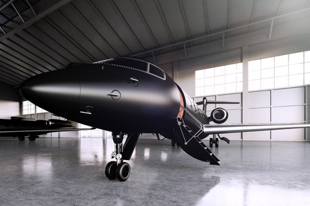 Closeup photo of Black Matte Luxury Generic Design Private Jet parking in hangar airport. Concrete...
