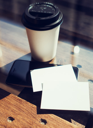 Two Blank White Business Card Mockup Wood Table Take Away Coffee Cup Coworking.Modern Phone Ready Work Office Blurred Background.Clean Object Private Corporate Information.Vertical Hot Drinks Mock Upの写真素材