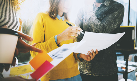Three young colleagues discussing business strategy.Woman holding papers in her hands and showing document near the window. Blurred, horizontalの写真素材