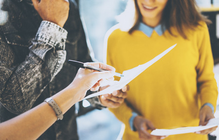 Closeup of man holding the papers in his hands and woman signing document. Coworkers team working in sunny office near the window.Horizontal, blurred backgroundの写真素材