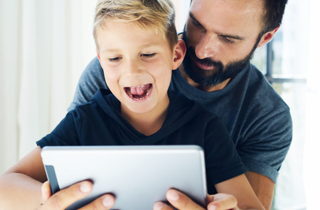 Closeup of young boy sitting with father at the table and using pc tablet in modern loft. Horizontal, blurred backgroundの写真素材