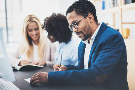 Three young coworkers working together in a modern office.Man wearing glasses, jacket and making notes in a document.Horizontal,blurred background.の写真素材