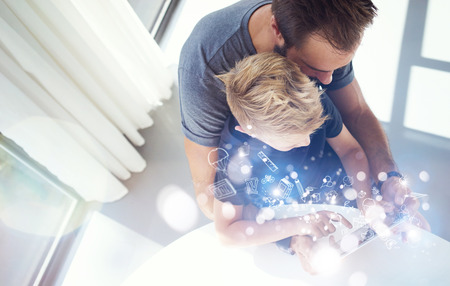 Dad and little boy playing together on mobile computer PC tablet, resting in modern house.Childhood dreams icons concept.Horizontal, blurred background. Top viewの写真素材