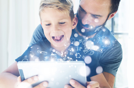 Closeup photo of young boy sitting with father at the table and using pc tablet in modern house.Childhood dreams icons concept.Vertical, blurred backgroundの写真素材