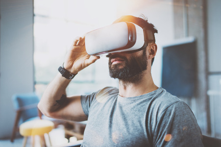 Bearded man wearing virtual reality glasses in modern interior design coworking studio. Smartphone...