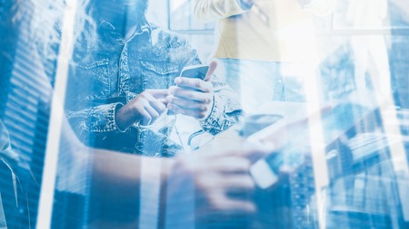 Double exposure concept.Closeup of young coworkers using electronic gadgets in sunny loft.Man holding a smartphone his hands,touching screen.Skyscraper office building blurred background.Horizontalの写真素材