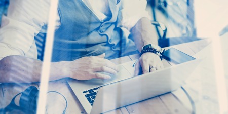 Concept of young successful businessman wearing a classic waistcoat and working at the wood table in modern coworking place.Double exposure,skyscraper office building on the blurred background.Wideの写真素材