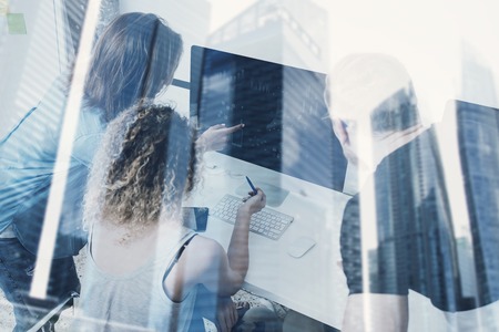 Group of young people working on computer in modern coworking studio.Coworkers using electronics gadgets.Icons,graphs and diagramm monitor.Double exposure,skyscraper building,blurred backgroundの写真素材