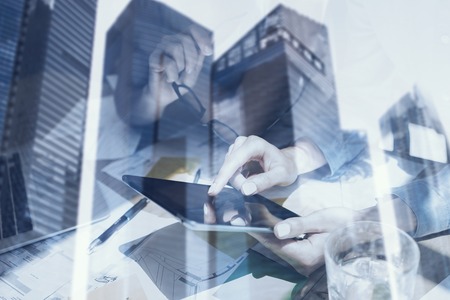 Closeup view of female hands touching screen electronic tablet.Concept business people using mobile gadgets.Double exposure,modern skyscraper office building on blurred background.Horizontalの写真素材