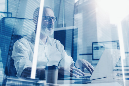 Concept of adult bearded businessman wearing a classic glasses and working at the wood table with...