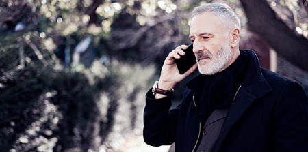 Attractive middle age businessman calling smartphone while spending time in a urban park.Horizontal wide,blurred background.の写真素材