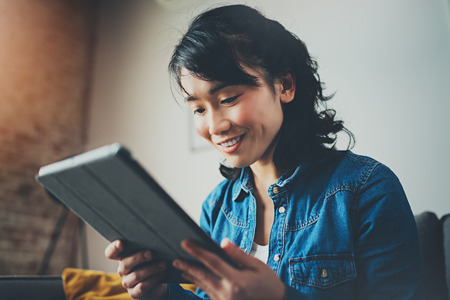 Young smiling Asian woman spending rest time at home and using digital tablet for video conversation with friends.Blurred background, flares effect.の写真素材