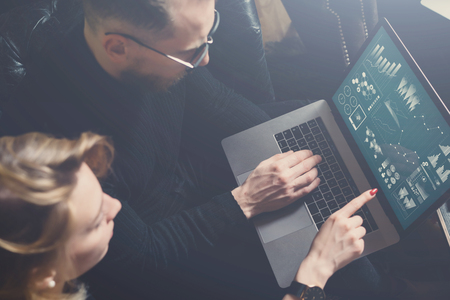 Coworking process in office.Two young colleagues using computer.Woman wearing black pullover and sitting on the sofa.Graphs,online interfaces and diagramm on laptop screen.Horizontal, color filter.の写真素材