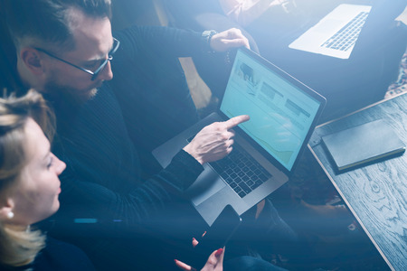Coworking process in office.Two young colleagues using computer.Woman wearing black pullover and sitting on the sofa.Graphs and diagramm on laptop screen.Horizontal, visual effects.の写真素材