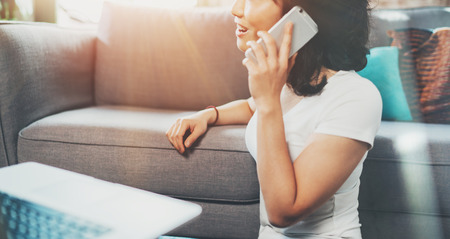 Attractive smiling Asian woman spending time at home on sofa and using smartphone for making call.Blurred background, flares effect.の写真素材