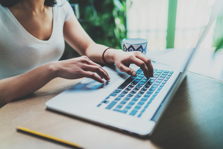 Closeup view of young woman working at home on modern computer.Female hands typing on laptop keyboard while sitting at the wooden table.Blurred background.の写真素材
