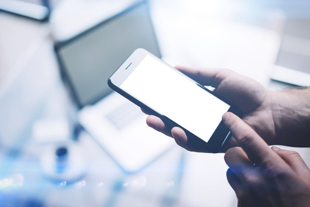 Closeup view of man hands holding modern mobile phone with white clean screen and pointing finger to...