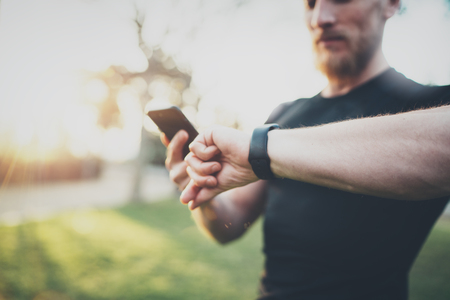 Muscular bearded athlete checking burned calories on smartphone application and smart watch after good workout session on city park.Blurred background.Selective focus on hand.の写真素材