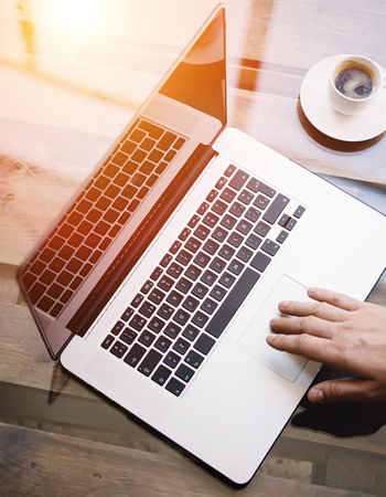 Man working with laptop at sunny office.Male hand pointing on notebook trackpad.Modern notebook, cup of black coffee on the wooden table.Reflections on glass surface.Vertical.Top view.Visual effect.の写真素材