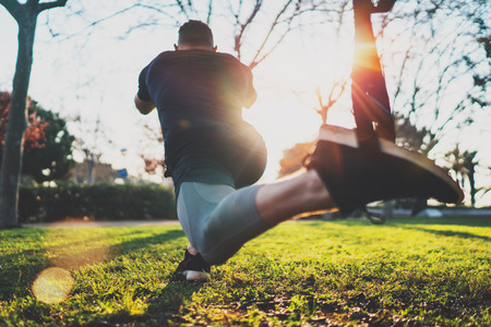 Feel your strength concept.Rear view of young athlete exercising trx outside in sunny park.Great TRX workout.Handsome man in sportswear doing exercising outdoors.Blurred background,flare.の写真素材