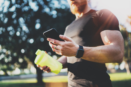 Workout smart fitness concept.Young Muscular athlete checking training programm on smartphone application after perfect workout session at sunny morning.Blurred background.の写真素材