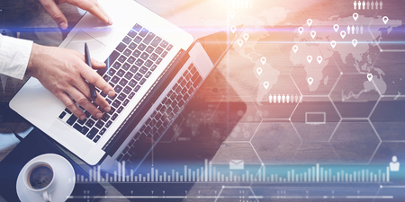 Concept of digital screen,virtual connection icon,diagram,graph interfaces.Businessman working with laptop at office.Modern notebook,cup of black coffee on wooden table.Sunlight effect glass surface.の写真素材