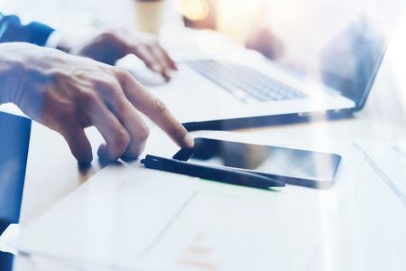 Man working on modern mobile phone at office and pointing finger to home button.Horizontal closeup view, blurred background, visual effects.の写真素材