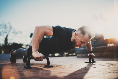 Handsome young sport man doing pushups in the park on the sunny morning.Healthy lifestyle concept.Training outdoors.Blurred background.の写真素材