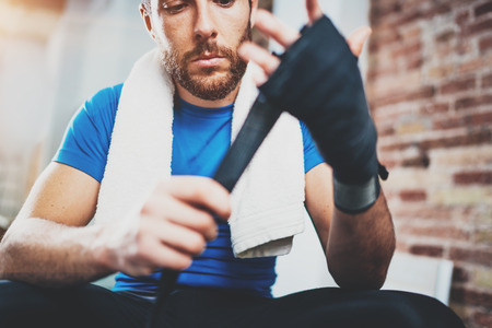 Young athlete tying black boxing bandages.Boxer man concentrating before kickboxing training. Blurred background. Horizontal.の写真素材