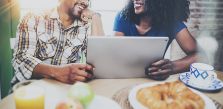 Happy african american couple are having breakfast together in the morning at the wooden table.Smiling black man and his girlfriend using touch tablet on breakfast at home.Wide.の写真素材