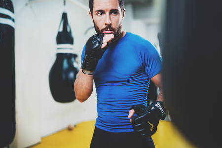 Concept of a healthy lifestyle.Young muscular man fighter practicing kicks with punching black bag.Kick boxer boxing as exercise for the fight.Boxer hits punching bag in gym.Horizontal.の写真素材