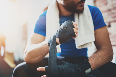 Muscular young boxer with black boxing bandages. Fists of fighter before the fight or training in sport gym. Blurred background. Horizontalの写真素材