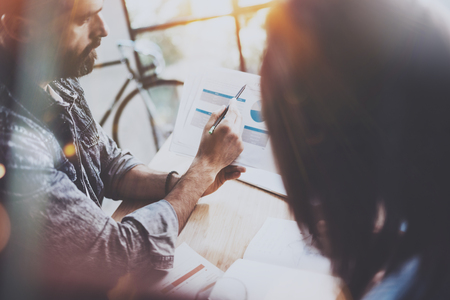 Young coworkers working together in modern office.Bearded man talking with colleague and showing paper documents.Business people brainstorming concept.Horizontal.Blurred background.Flaresの写真素材