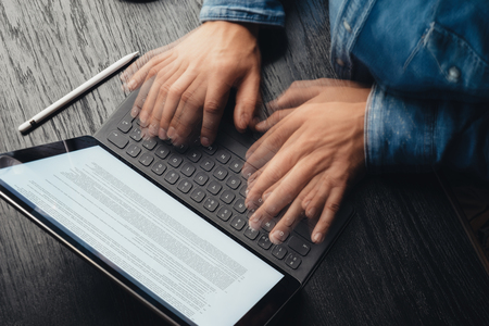 Closeup view of male hands fast typing on electronic tablet keyboard-dock station. Business...