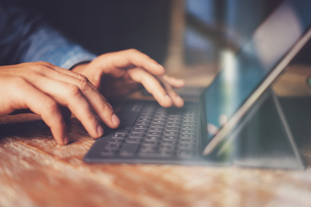 Male hands typing on electronic tablet keyboard-dock station.Man working at office while sitting at...