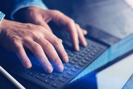 Closeup view of male hands typing on electronic tablet keyboard-dock station. Businessman working at...