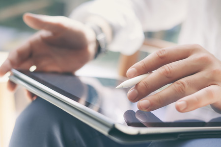 Closeup view of coworker holding digital tablet on hand and using electronic pen while working at office.Pointing tablet screen.Blurred background.Horizontal.の写真素材