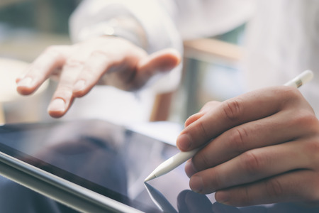 Closeup view of male hands holding digital tablet on hand and using electronic pen while working at sunny office.Stylus pointing tablet screen.Blurred background.Horizontal.の写真素材