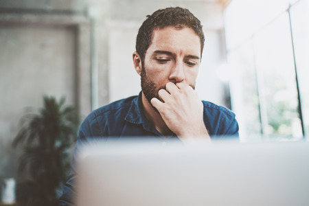Young Businessman working at modern loft office.Pensive Man sitting and using contemporary laptop.Blurred background.Horizontalの写真素材