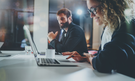 Coworkers working process photo.Smiling girl in eye glasses working together with bearded colleague at night modern office loft.Teamwork concept.Blurred background.Horizontal.の写真素材