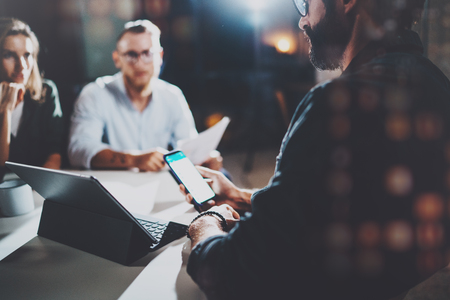Coworkers working together in modern office.Bearded man talking with colleague and using mobile laptop while sitting at the wooden table.Horizontal.Blurred background.Flares.の写真素材