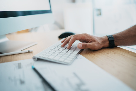 Male hand typing on computer keyboard.Blogger working at studio while sitting at wooden table.Horizontal.Blurred background.の写真素材