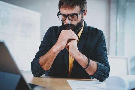 Closeup of bearded male architect wearing eye glasses working on a digital tablet dock at his desk. Professional experienced engineer constructionist developer.Horizontal.Blurred background.の写真素材