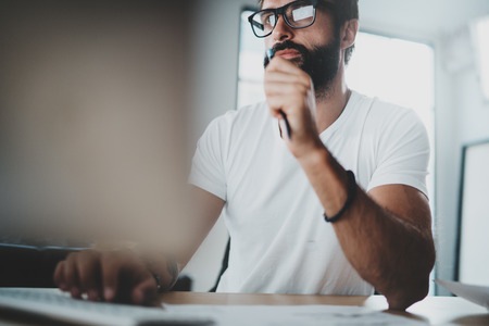 Pensive bearded coworker wearing eye glasses and working at modern loft studio-office.Blurred background. Horizontal.の写真素材
