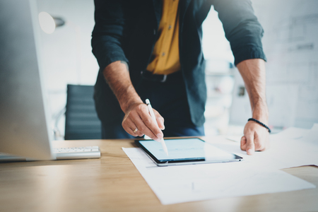Close up view of man in formal wear working with portable tablet computer and drawings digital plans in modern lightful office.Horizontal.Blurred background.の写真素材