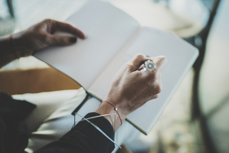 Beautiful young woman writing something in note pad while sitting on armchair at living room.Charming female studying doing homework at home.Horizontal.Blurred background.の写真素材